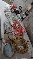 Photo showing a variety of cords and lights laid out on a flat surface, highlighting a yellow extension cord, red and black flashlights, and power bars with multiple outlets.