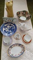 Overview of all items in the lot arranged on white cloth showing teapots, teacups, plates, and decorative bowls.