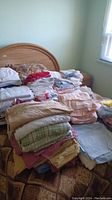 Multiple stacks of assorted linens including sheets, pillowcases, and towels on a bed.