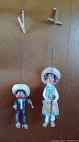 Two marionette puppets hanging side by side, showing overall full view including their strings and cross hangers