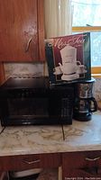 View of all three appliances on kitchen counter: black Hamilton Beach microwave oven, boxed Mrs. Tea tea maker on top, and Oster coffee maker.