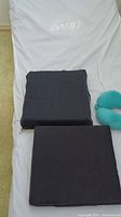Two black square Roho wheelchair cushions and one teal neck cushion on a white mattress