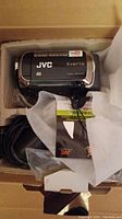 Top view of the JVC Everio memory camera inside the box with cables and manuals visible.