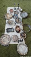Wide view of approximately 20 assorted silver pieces spread on a surface showing candlesticks, trays, covered dish, and small bowls.