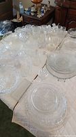 Various clear glass and crystal bowls, platters, vases, and decanters arranged on table covered with white quilted fabric.
