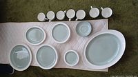 View of multiple plates, an oval platter, cups and saucers arranged on a cloth showing the sage and white Wedgwood china set.