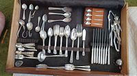 Photo showing arranged silverplate cutlery pieces laid on dark fabric including various forks, spoons, knives and small boxed set of spoons.
