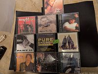 10 music CDs laid out on black surface, showing front covers featuring various artists including Boney M, Aaron Neville, Brad Paisley, John Michael Montgomery, and Patty Loveless.