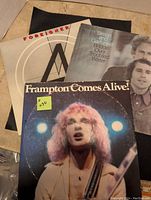 Three vinyl record covers displayed, showing Foreigner, Simon & Garfunkel, and Frampton Comes Alive album artwork.