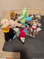 Photo showing seven Coca Cola stuffed animals arranged on black background. Various animals including toucan, peacock, monkey, and others visible.