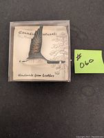 Front view of the leather brooch shaped like a Canada Goose flying, attached to a display card with brand and material info.