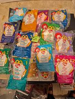 Top-down photo of all 12 Teenie Beanie Babies in original McDonald's packaging, numbered 1 to 12, arranged on floor with McDonald's branding visible on cards.