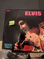 Front cover of the Elvis Good Times vinyl record album showing Elvis singing into a microphone wearing a white costume with rhinestones.