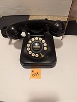 Front view showing rotary dial with numbered buttons and handset on cradle.