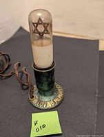 Jewish in memory electric light with clear glass bulb housing a Star of David symbol, green metal base inscribed with 'IN LOVING MEMORY', unplugged and off.