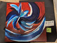Photo of the abstract art painting showing swirling blue and red colors and tag attached.