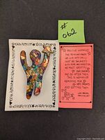 Brooch in a shaped positive woman figure with colorful abstract design on a white card with repeated text of artist's name, next to a coral pink card with handwritten inspirational quote.