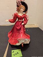 Front side view of Royal Doulton Patricia figurine showing red dress and feathered black hat.