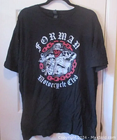 Full front view of black Forman Motorcycle Club T-shirt hanging, showing general shape and color.