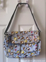 Front view of the Harajuku Lovers crossbody bag hanging on door showing front flap, two mini front pockets, and adjustable black strap.