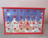 Front view of Kurt Adler wooden advent calendar showing 24 numbered drawers with red knobs and handpainted Christmas village scene.