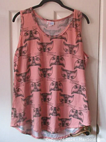 Full view of the sleeveless blush pink tank top with black cat face prints hung on a hanger against a door.