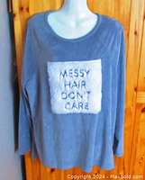 Front view showing grey plush material with white faux fur panel embroidered 'MESSY HAIR DON'T CARE'. Shows long sleeves and rounded neckline.