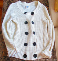 Front view of white chunky knit cardigan showing double breasted large black buttons and ribbed cuffs and hem.