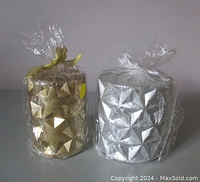 Pair of wrapped shimmery holiday pillar candles in gold and silver with geometric star pattern.