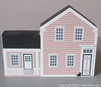 Front and side view of wooden shelf sitter replica of Lillian Gish Home with pink siding and black roof, featuring detailed doors, windows, and a small black cat near front door.