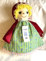 Doll showing Little Red Riding Hood with yellow curly yarn hair, red cape and green patterned dress with lace trim.