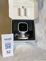 Front view of the Blink Mini camera in its packaging, showing the camera, USB cable, and mounting base.