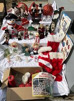 Full view of the assorted Christmas decorations arranged on a white cloth showing handmade snowmen, angels, nutcrackers, stockings, large red balls, and candles.