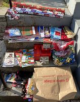 Wide assortment of Christmas wrapping supplies including rolls of wrapping paper, gift bags, gift tags, boxes, and cards arranged on outdoor steps.