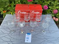 Front view of the eight crystal wine glasses arranged with two original red Prestige Boxes behind them, outdoors on a table with floral background.