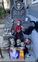 Overview of Halloween decorations on steps showing tombstones, skeleton figure, black cat, skeleton lights, spiderweb lights with pumpkin and ghost shapes, and sealed ghost window clings.