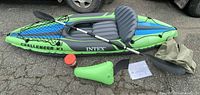Full view of inflated kayak with front net, paddle, seat, foot rest, pump, and boating kit laid out on ground.