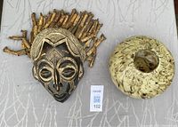 Top-down photo of African style carved mask and a large decorative glass bowl placed side by side on a light colored surface.