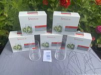 Five white boxes of Spiegelau Capri long drink glasses with two glasses displayed in front, arranged outdoors on a cloth with flowers in the background.