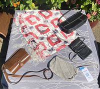 White scarf with red geometric and black ring pattern, glossy black purse with wrist strap, brown wallet-style purse, light gray suede wristlet pouch on display outside