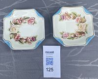 Front view of two octagon-shaped ceramic side plates with rose floral wreath designs, light blue borders and gold accents.