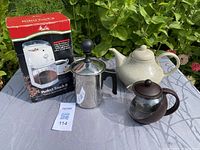 Full lot view with coffee grinder in box, stainless steel milk frother, large beige ceramic teapot, small glass teapot with brown handle and filter.