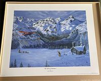 Full view of the framed/art print in an open box showing snowy mountainous scene with airplane, log cabin, man and dog sled.