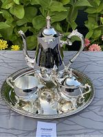 Front angled view of the four piece silver plate tea set on the tray with foliage background