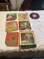Seven vintage 45 RPM records on bed, with colorful illustrated sleeves and some visible wear.