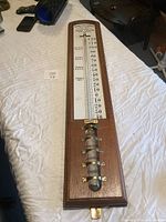 Full view of the antique wooden wall thermometer showing the temperature scale and brass fittings.