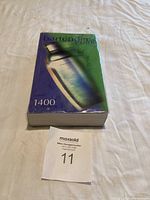 Front cover of bartender's guide book featuring a cocktail shaker and text showing over 1400 recipes.