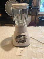 Full view of the Oster blender with glass jar and white lid on a table, showing overall item condition.