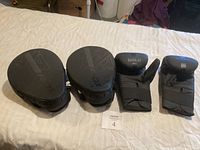 Photo showing a pair of black boxing gloves and two RDX focus mitts laid out on a bed.