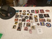 Wide view of black felt hat and concert pins laid out on fabric including The Who, Bruce Springsteen, Tina Turner, and others